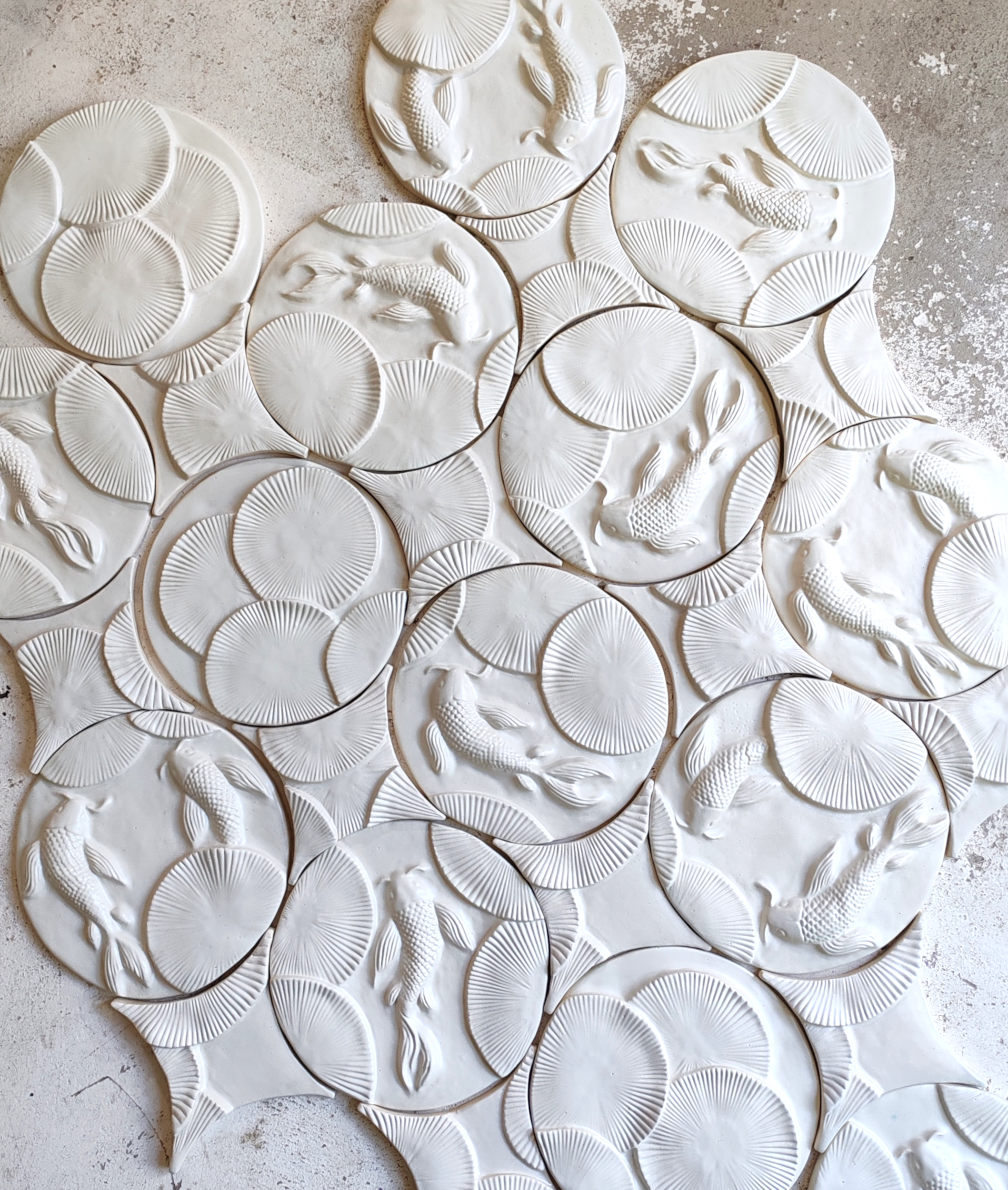 Textured handmade satin white ceramic wall tile featuring three-dimensional koi fish and lily pad relief patterns, crafted from natural clay for luxury interior design.